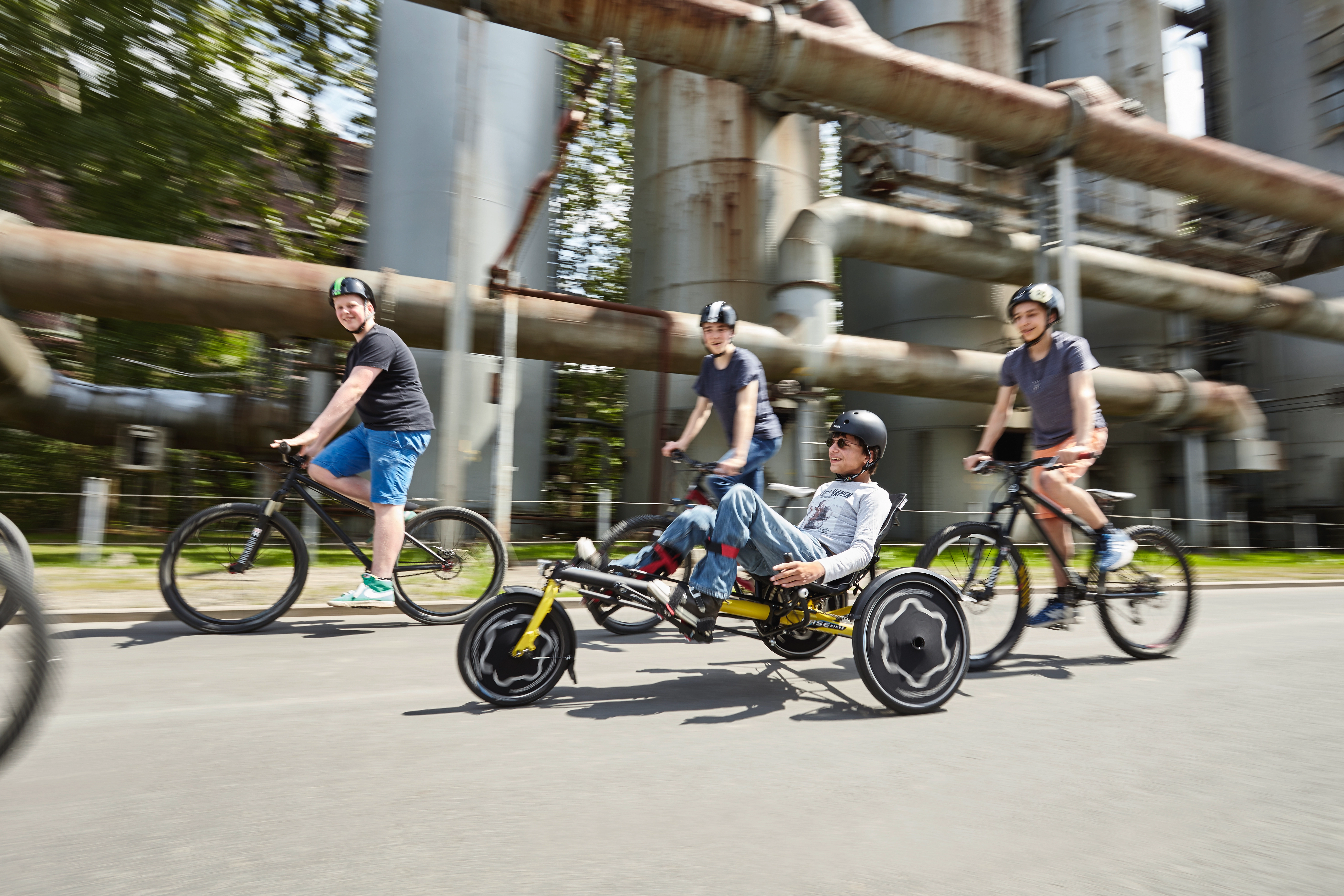 Gruppe Jugendlicher fährt gemeinsam Fahrrad, einer auf einem sportlichen Liegedreirad und Fahrrad 